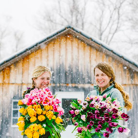 von Trapp Flowers famers holding large flower bouquets in front of a barn while it snows