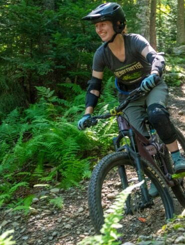 A women mountain biking with a guy behind her. Lots of ferns.