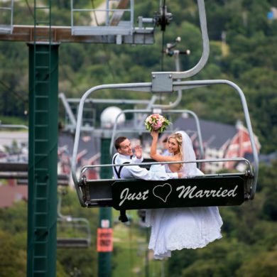 A married couple on the chairlift at Sugarbush with a 'Just Married' sign hanging behind them. Micro-weddings at Sugarbush