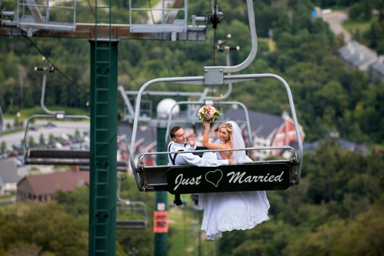 A married couple on the chairlift at Sugarbush with a 'Just Married' sign hanging behind them. Micro-weddings at Sugarbush